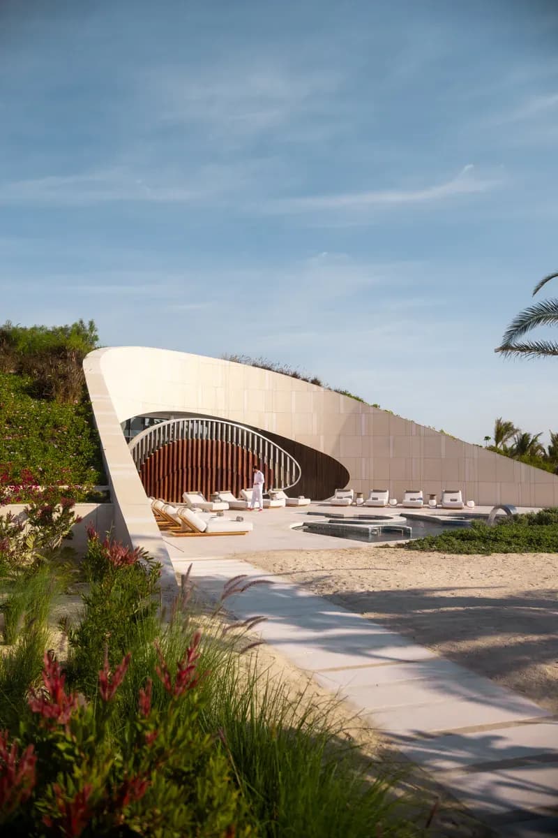 A sculpted stone pavilion arcs over the beach club, loungers and pools opening onto the sand.